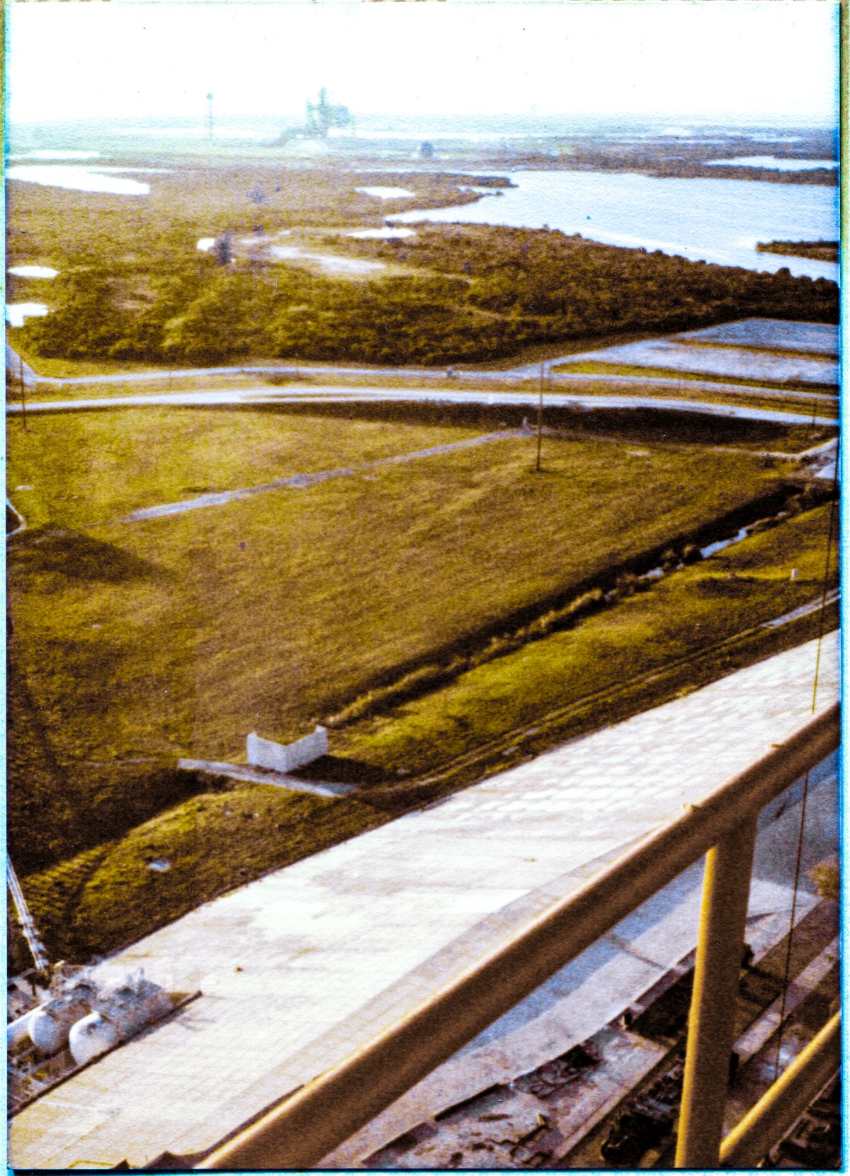 Image 041. In the golden light of a Florida Early Morning, the Space Shuttle Columbia sits poised in its launch position, supported by the Mobile Launch Platform which spans the Flame Trench at distant Launch Complex 39-A, Kennedy Space Center, Florida. You are seeing Columbia, prior to its first-ever mission, from a vantage point up on the Fixed Service Structure, high above the surrounding wilderness, at Pad B, which, at the time this photograph was taken, was still under construction, and had yet to host its own Shuttle launches. Photograph by James MacLaren.